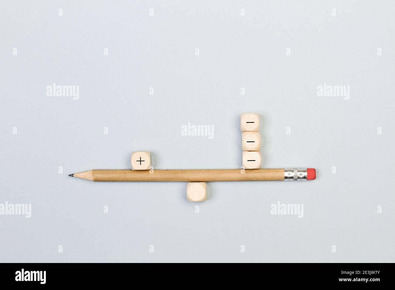 Minus and plus signs wooden cubes with a pencil in balance way on a gray background Stock Photo