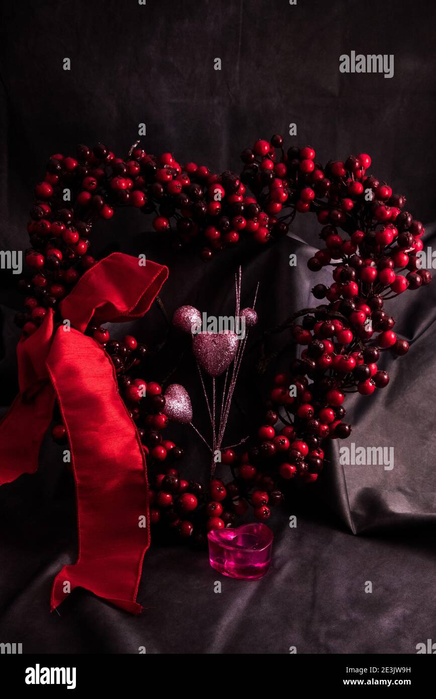 Heart shaped berry wreath and red bow against a dark background. Stock Photo