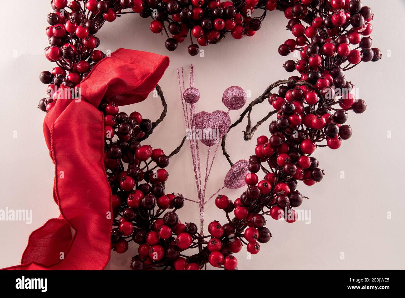 Heart shaped berry wreath and red bow against a white background. Stock Photo