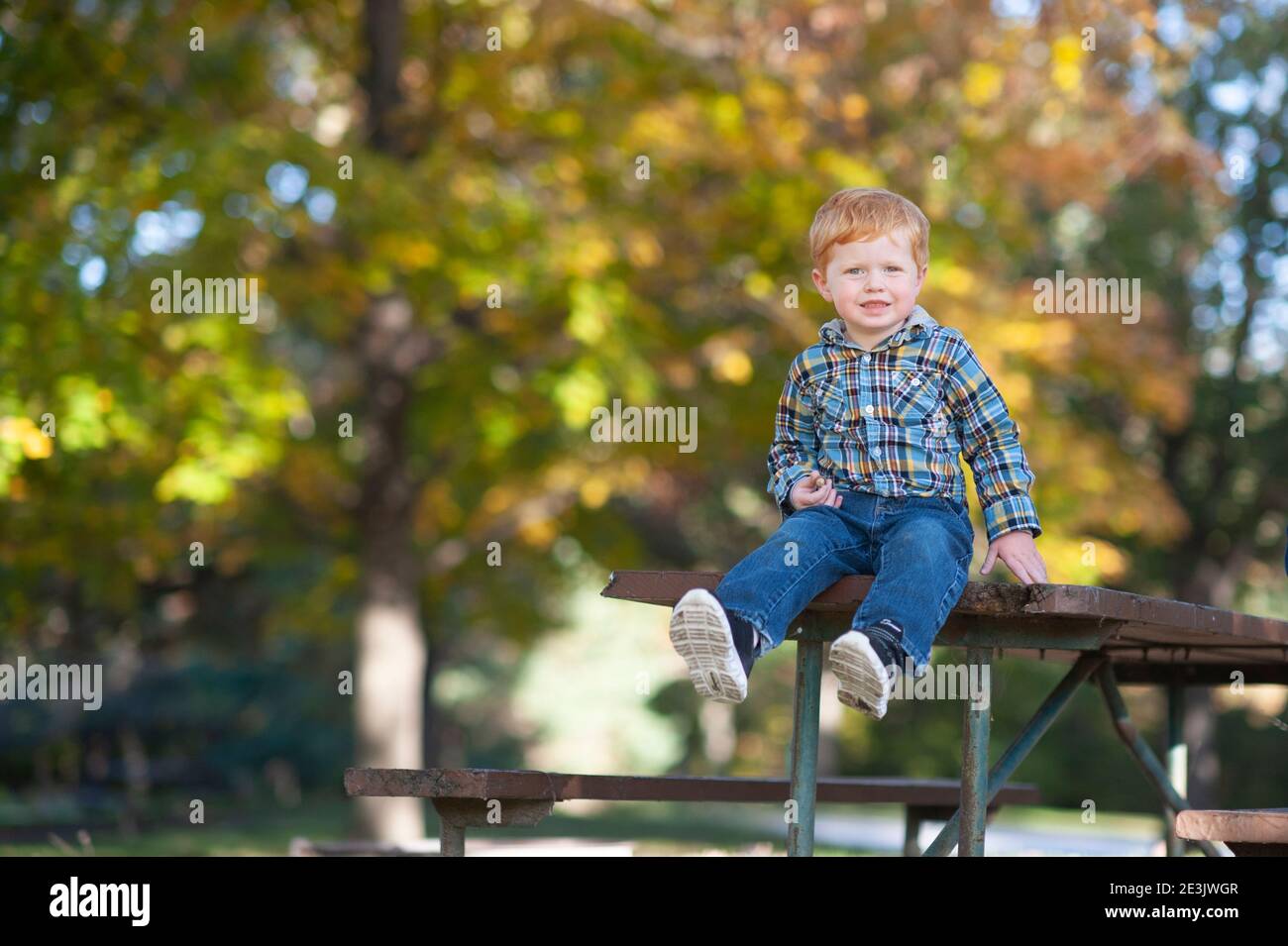 Toddler boy 3 to 4 years old sitting on edge of picnic table smiling Stock Photo