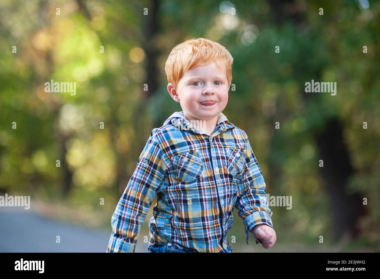 Close up of red haired toddler boy walking with tongue out outside Stock Photo
