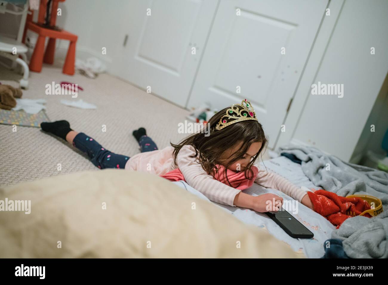 Young girl wearing tiara playing with smart phone laying down Stock Photo