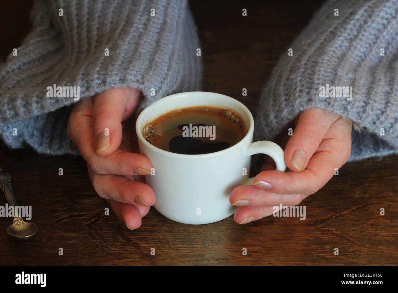 Woman's hands in sweater hold a cup of strong coffee on wooden table ...