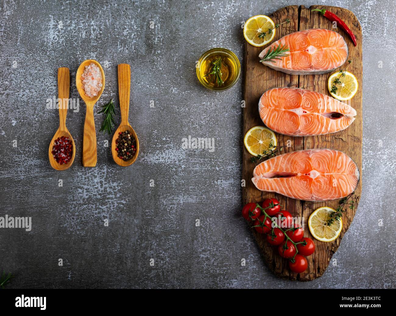 three raw steak fish trout, salmon and spices on wooden board, dark background Stock Photo