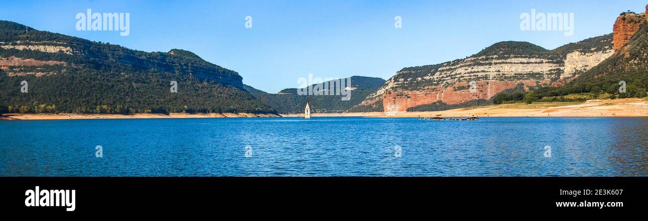 Panoramic landscape of the Sau swamp with its church. Tavertet and Collsacabra cliffs in the Sau Reservoir on a sunny day. Tourism in Osona, Barcelona Stock Photo