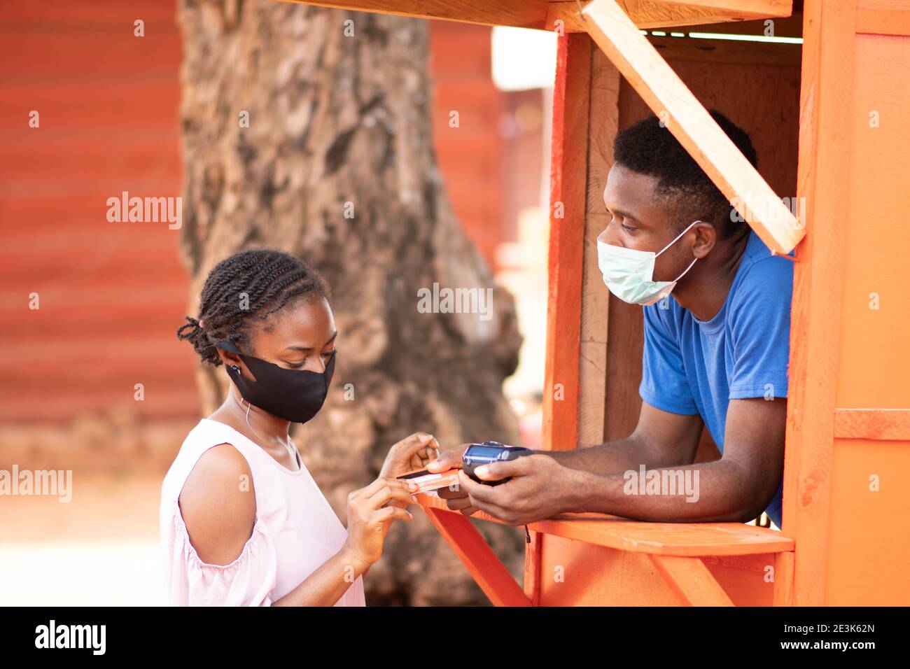 young nigerian woman at a pos service kiosk wanting to withdraw cash, wearing a face mask Stock Photo