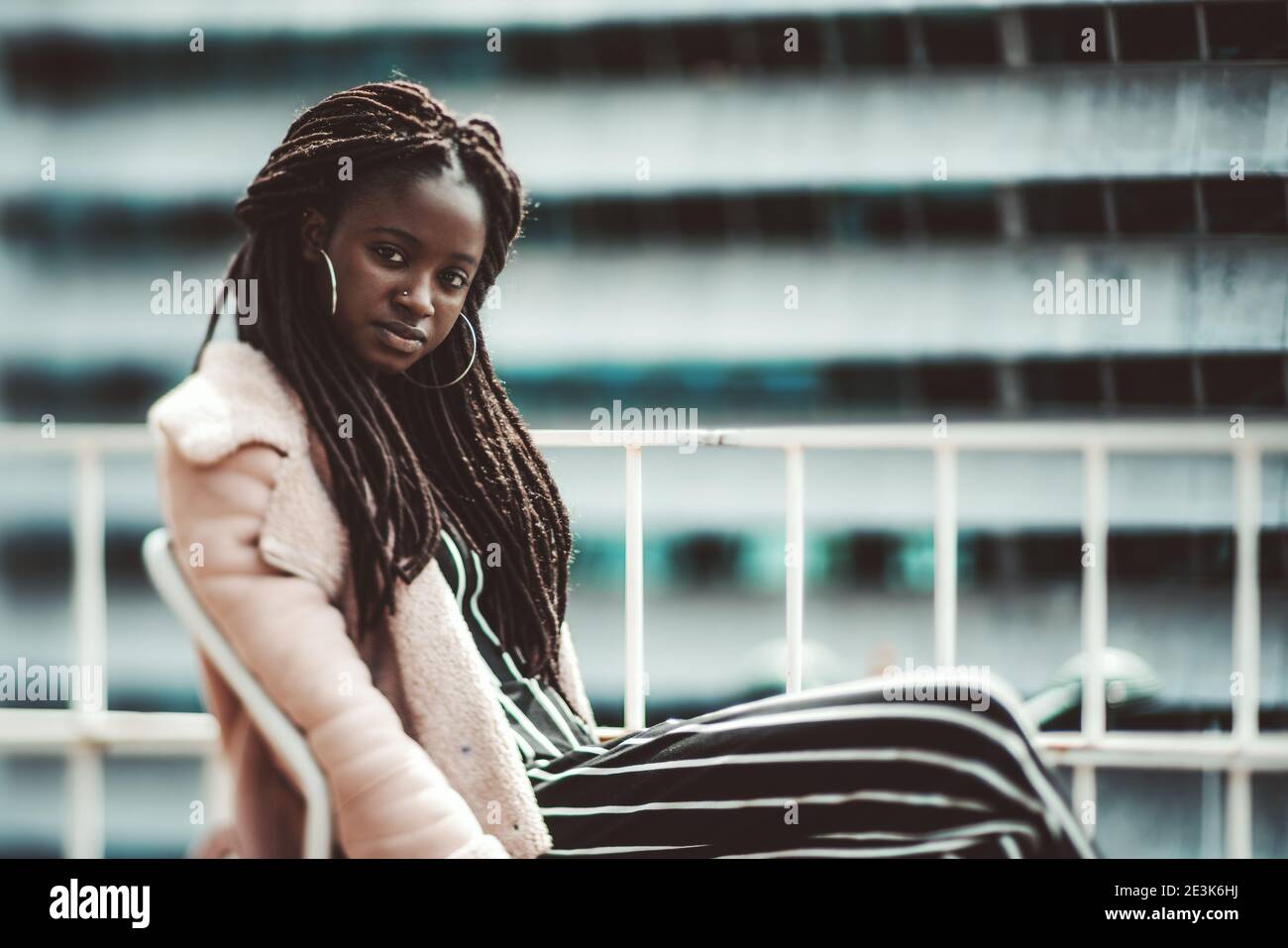 A true tilt-shift portrait with a selective focus on the part of the face and hair of a dazzling young black woman with a dreadlock sitting outdoors o Stock Photo