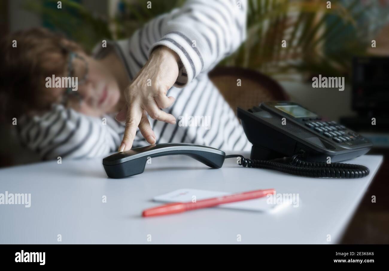 A very bored mature female waiting next to her hard line telephone, she 'walks' her fingers over the phone receiver. Stock Photo
