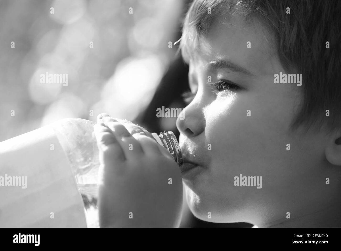 Child drinks water from a bottle while walking, baby health. Boy bottle of water. Young boy holding drink fresh water bottle. Black and white Stock Photo