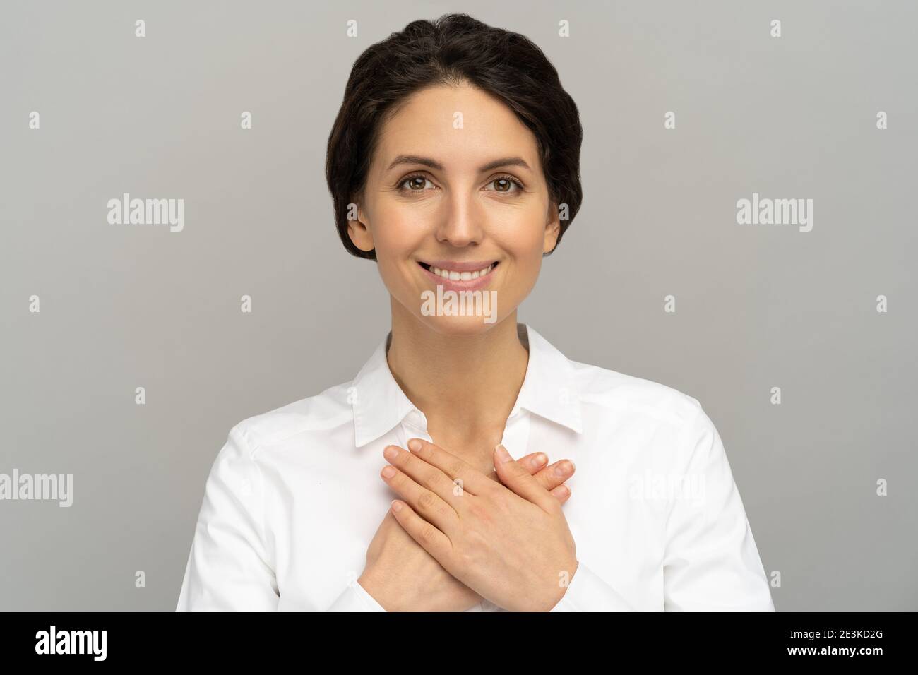 Friendly woman holds hands on chest, feels grateful for love, appreciation, thankful and support Stock Photo