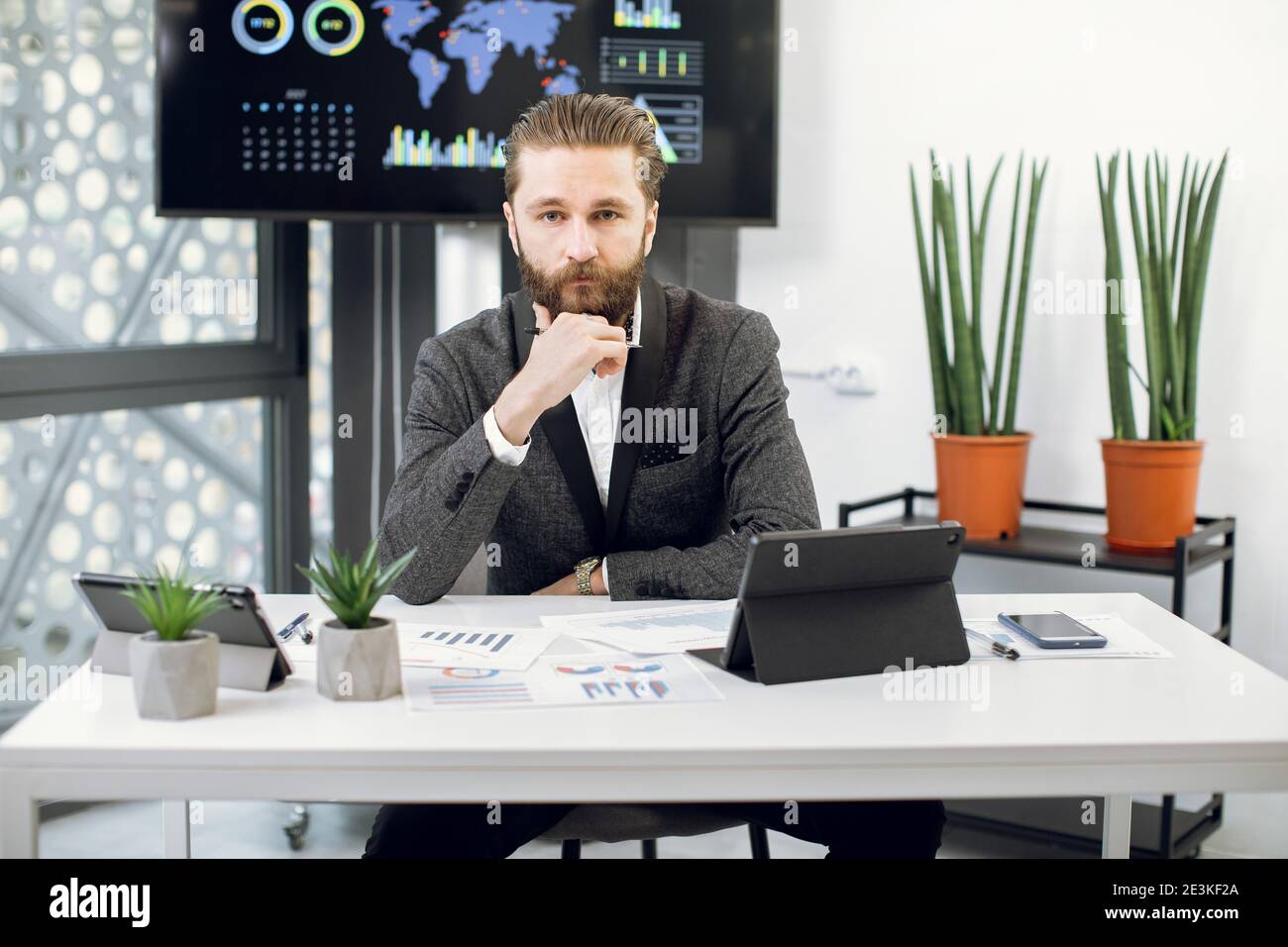 Handsome purposeful confident bearded businessman, chief executive officer in formal wear, sitting at workplace and looking at camera. Male worker Stock Photo