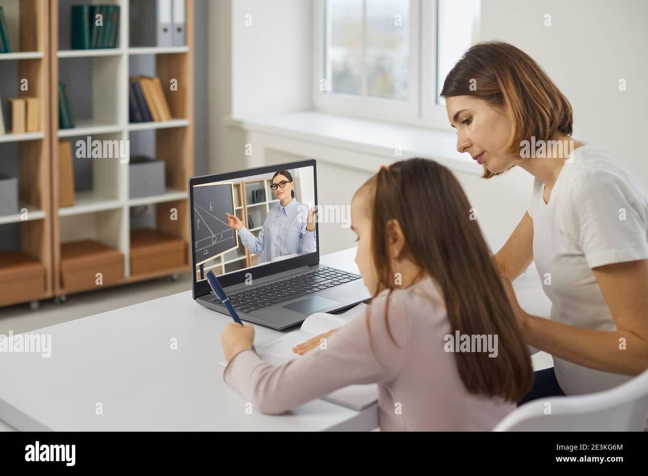 Mom helps her daughter in math by listening to a school teacher in an online lesson via video call. Stock Photo
