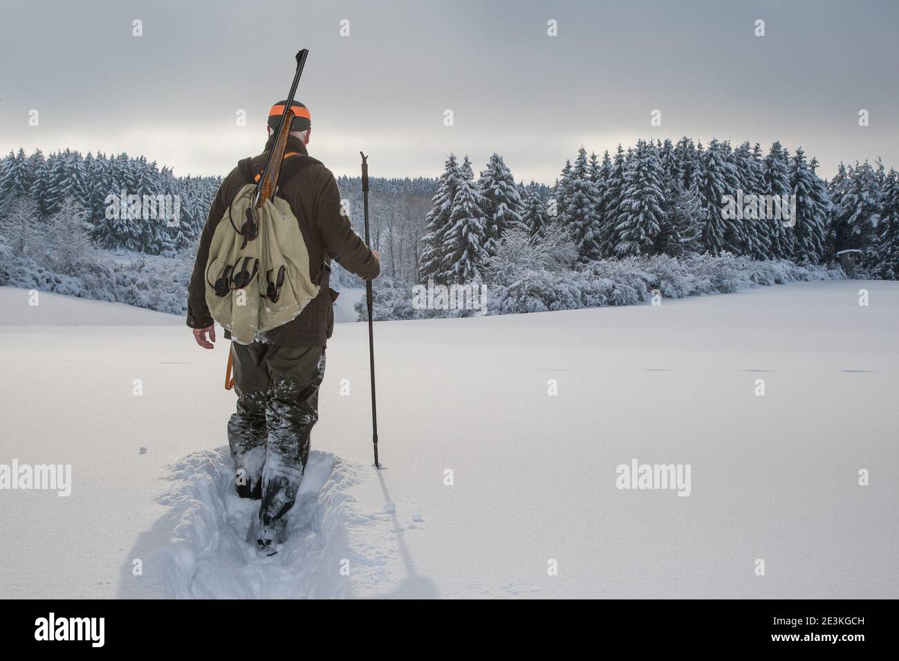 In a picturesque winter landscape a hunter walks down through the fresh, deep snow into the small valley. Stock Photo