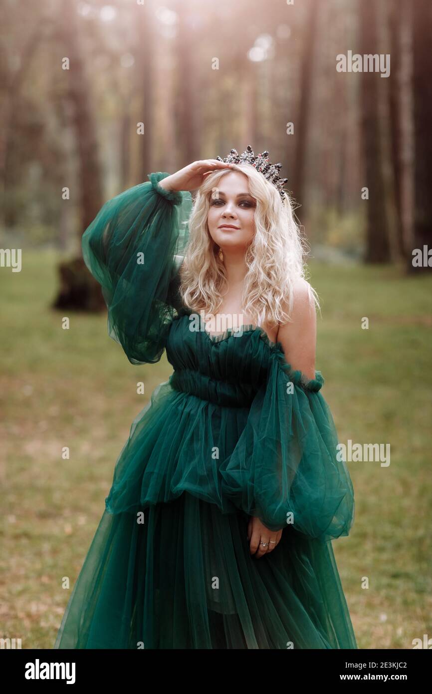young beautiful blonde hair woman queen. Princess walks. autumn green  forest mystic. Vintage medieval shiny crown. Long evening green dress.  magic fan Stock Photo - Alamy