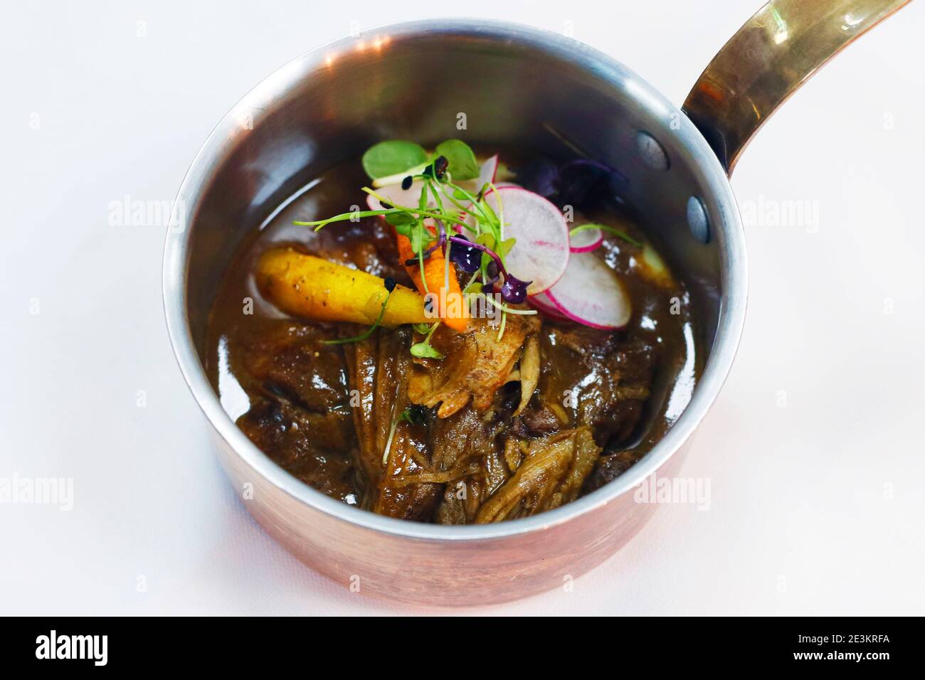 slow cooked pulled lamb shoulder in a coper pot with baby carrots and slice radish Stock Photo