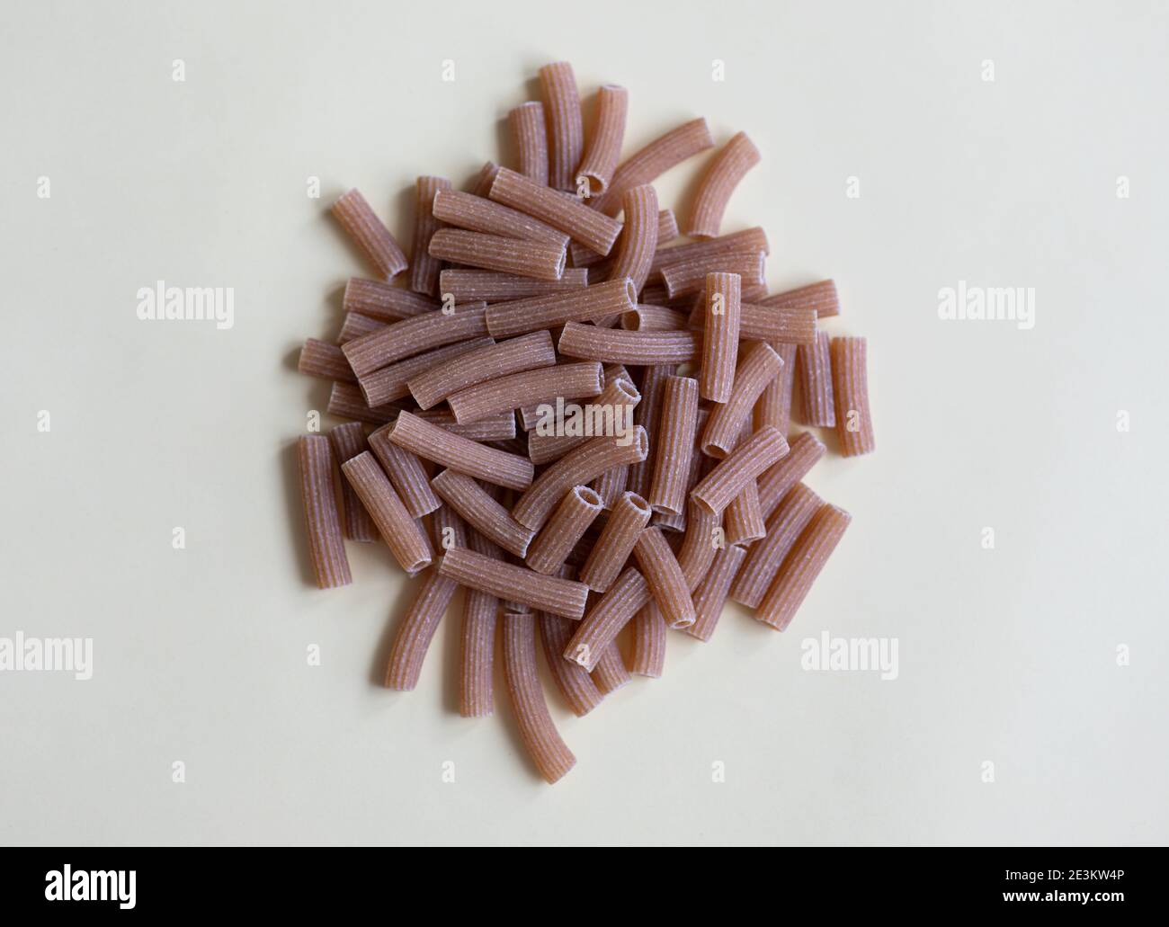 Raw whole grain brown pasta on a white background. Wholemeal pasta made of durum flour, rich in nutrients: protein, carbohydrates and fiber Stock Photo