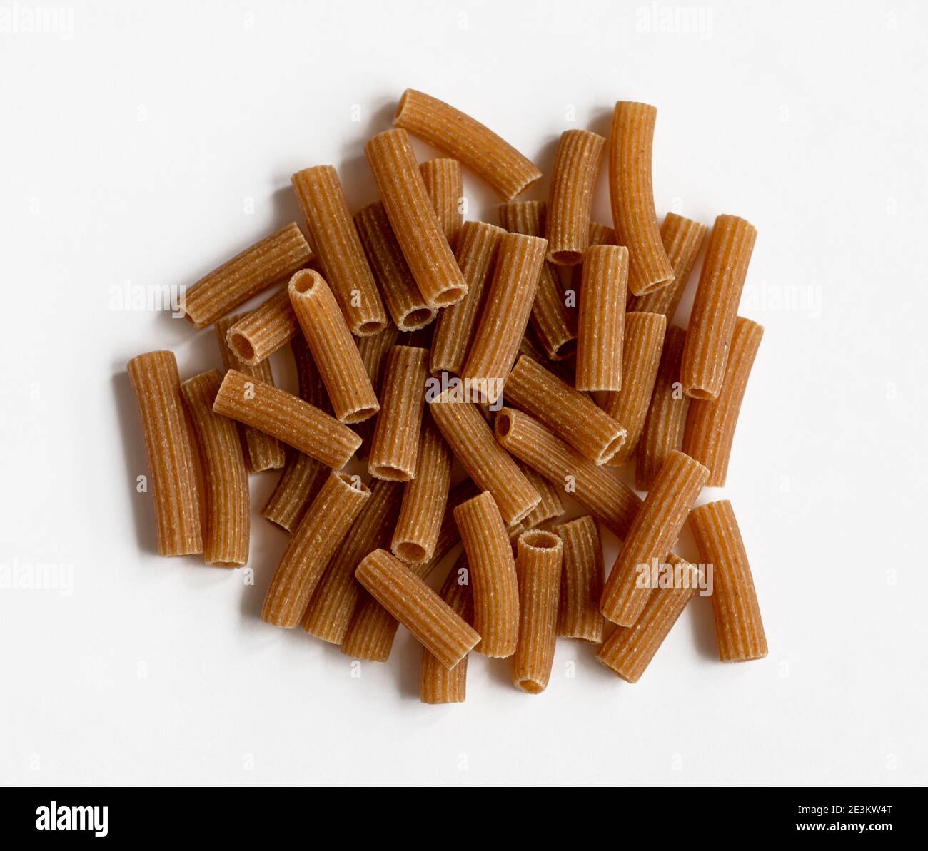 Raw whole grain brown pasta on a white background. Wholemeal pasta made of durum flour, rich in nutrients: protein, carbohydrates and fiber Stock Photo