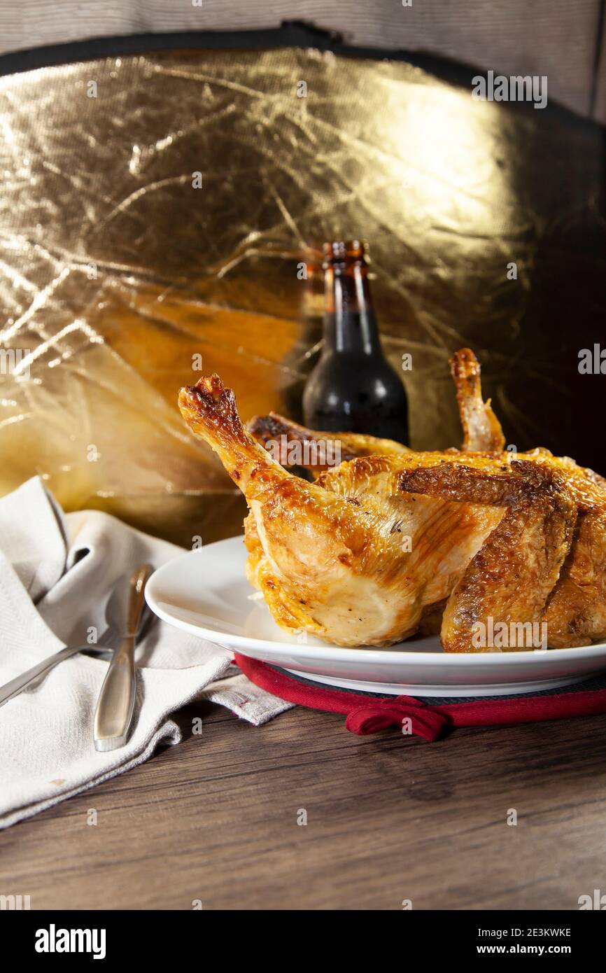 Whole roasted chicken on a white plate and a bottle of beer next to a grey napkin and silverware Stock Photo