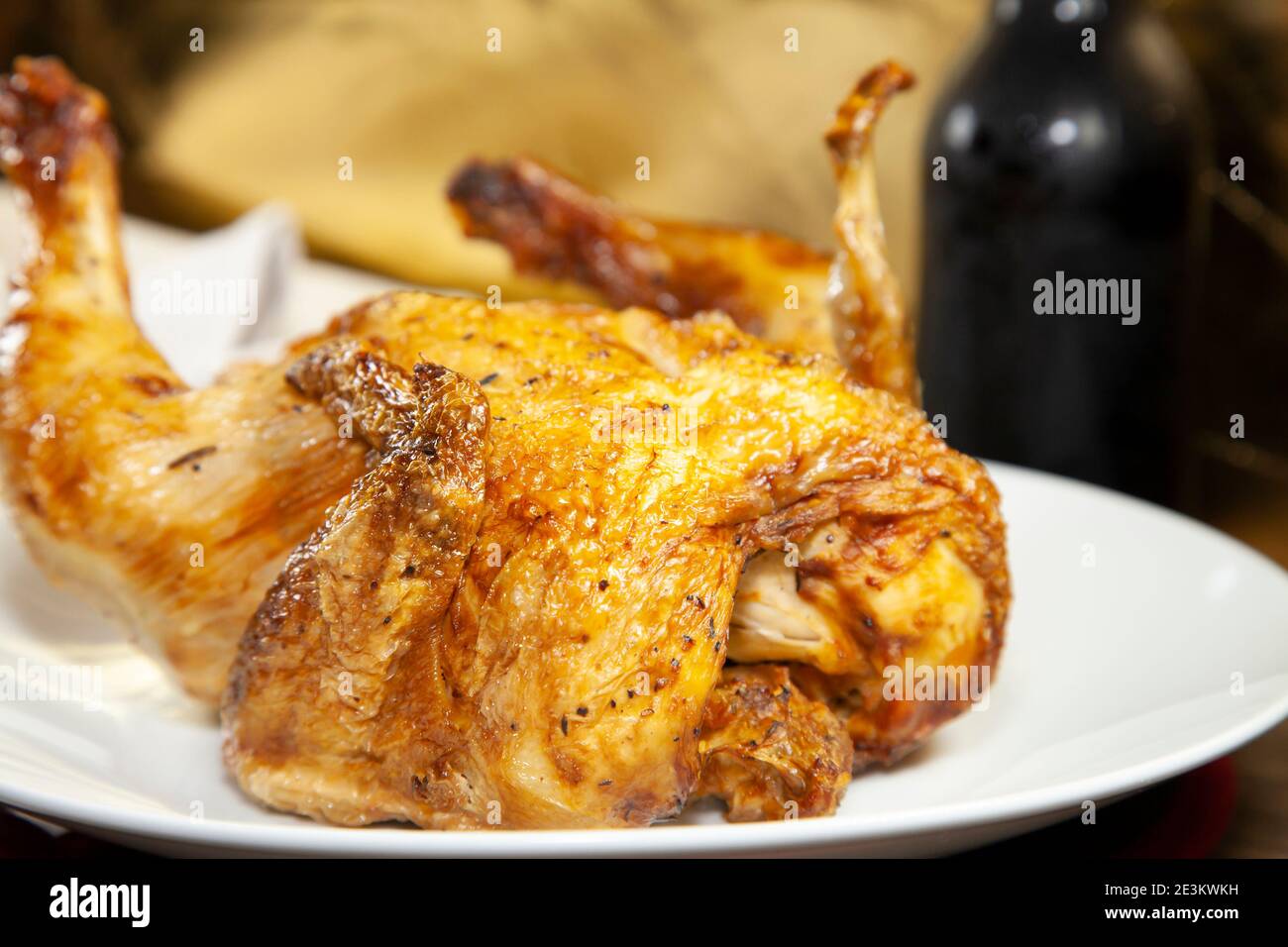 Whole roasted chicken on a white plate and a bottle of beer next to a grey napkin and silverware Stock Photo