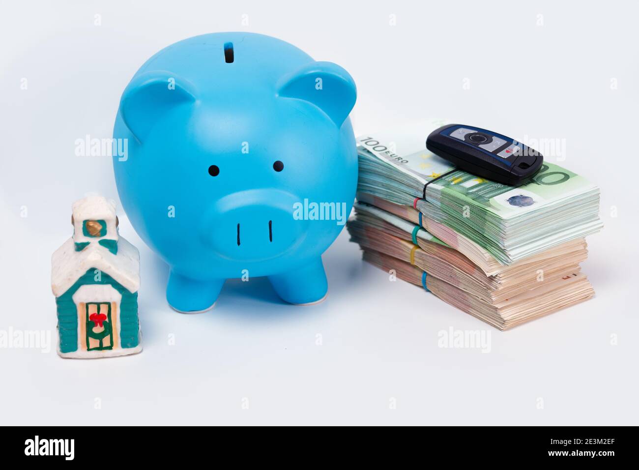 Stack pile of european money, Euro cash currency with a car key on it, a piggy bank next to it and a home on it isolated on white background. Savings Stock Photo