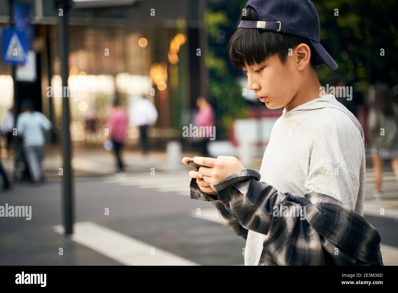 teenage asian child looking at cellphone while walking on street Stock Photo