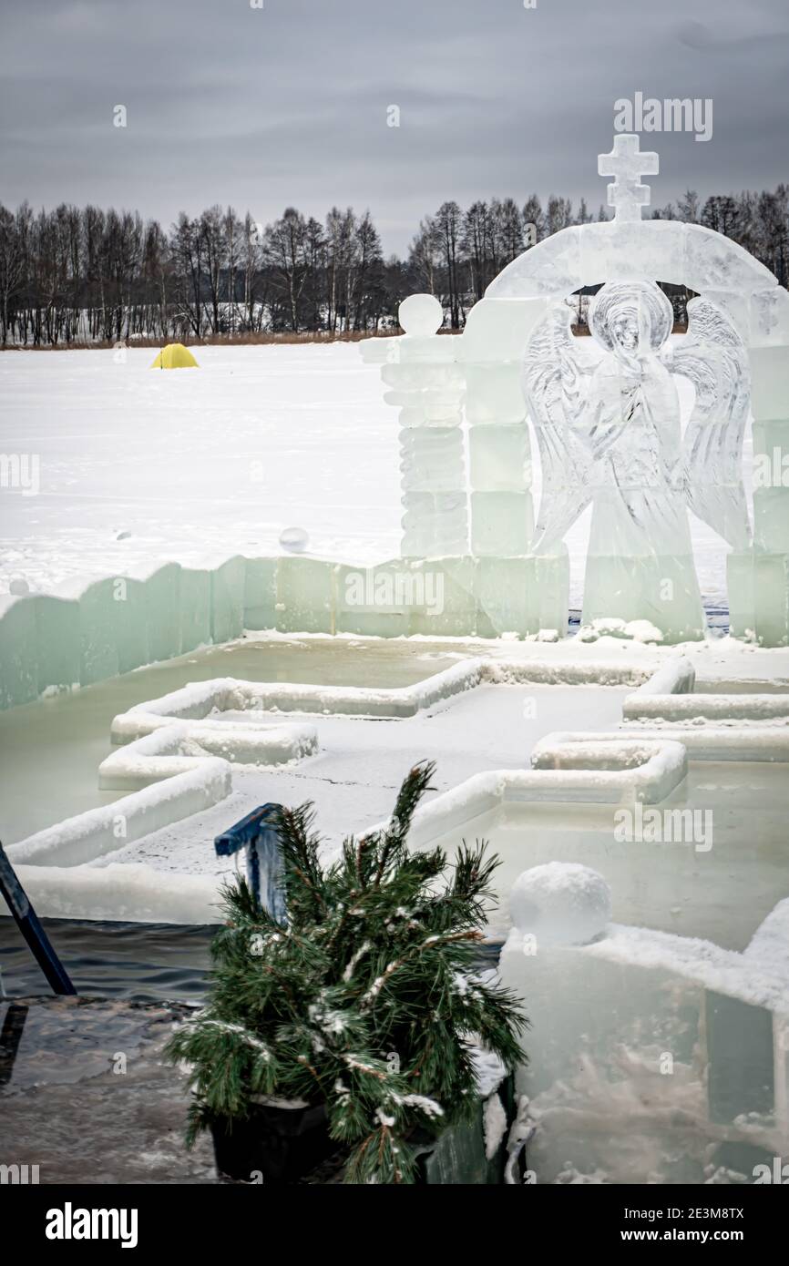 Font for dipping into an ice hole for the baptism of christ and ice sculpture in the form of an angel and a cross Stock Photo
