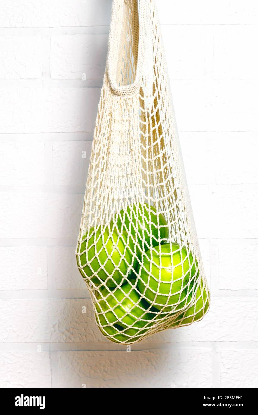 Fresh green apples in eco natural reusable cotton mesh bag. Zero waste concept. White brick background.  Stock Photo