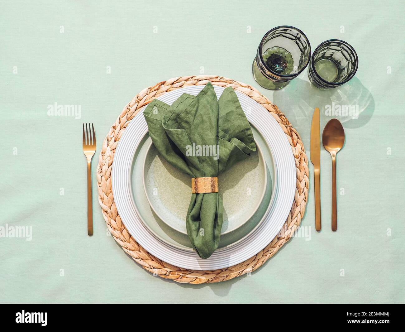 Beautiful festive table setting in green colors for St.Patrick's day with golden cutlery. Top view of Saint Patrick's day holiday table with green linen tablecloth and napkin, green glasses. Flat lay Stock Photo