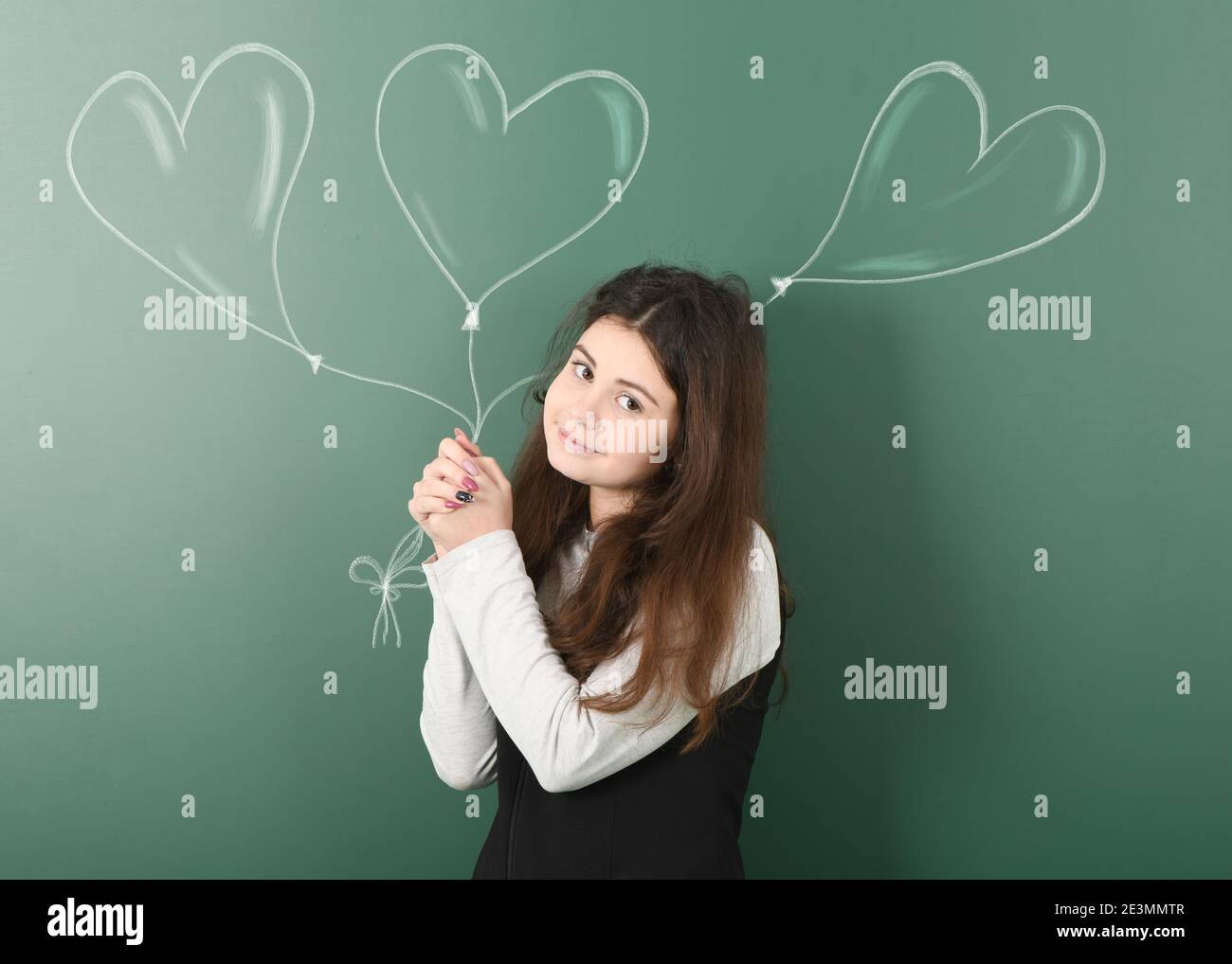 Pre-adolescent child holding three painted balloons on a green background. Balloons are heart-shaped. Stock Photo