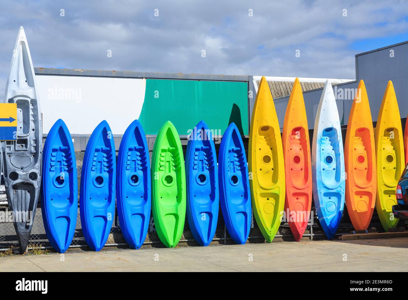 A row of plastic kayaks of various colors and sizes, lined up along a fence Stock Photo