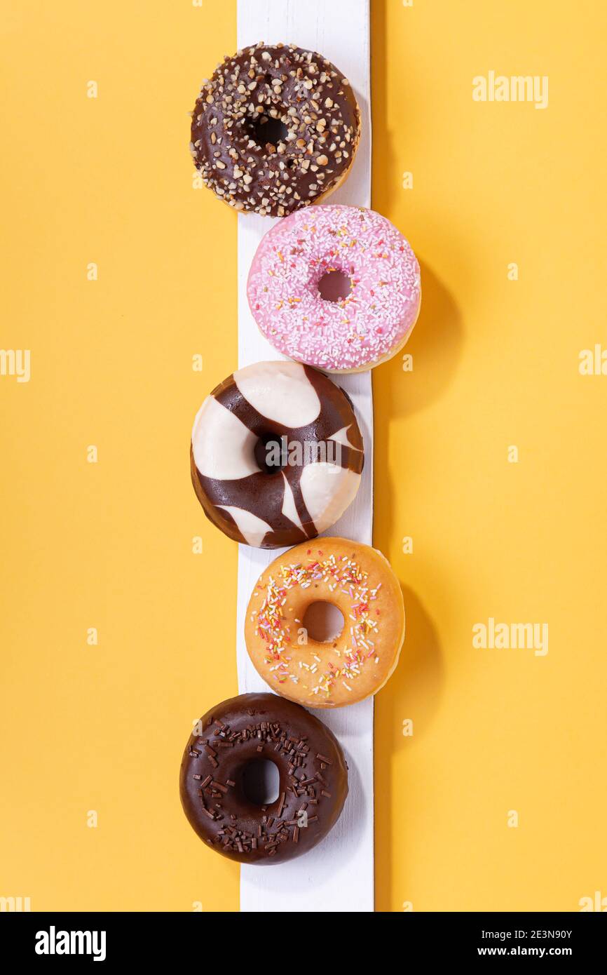 Flat lay composition with mixed donuts on yellow background. Vertical format. Stock Photo