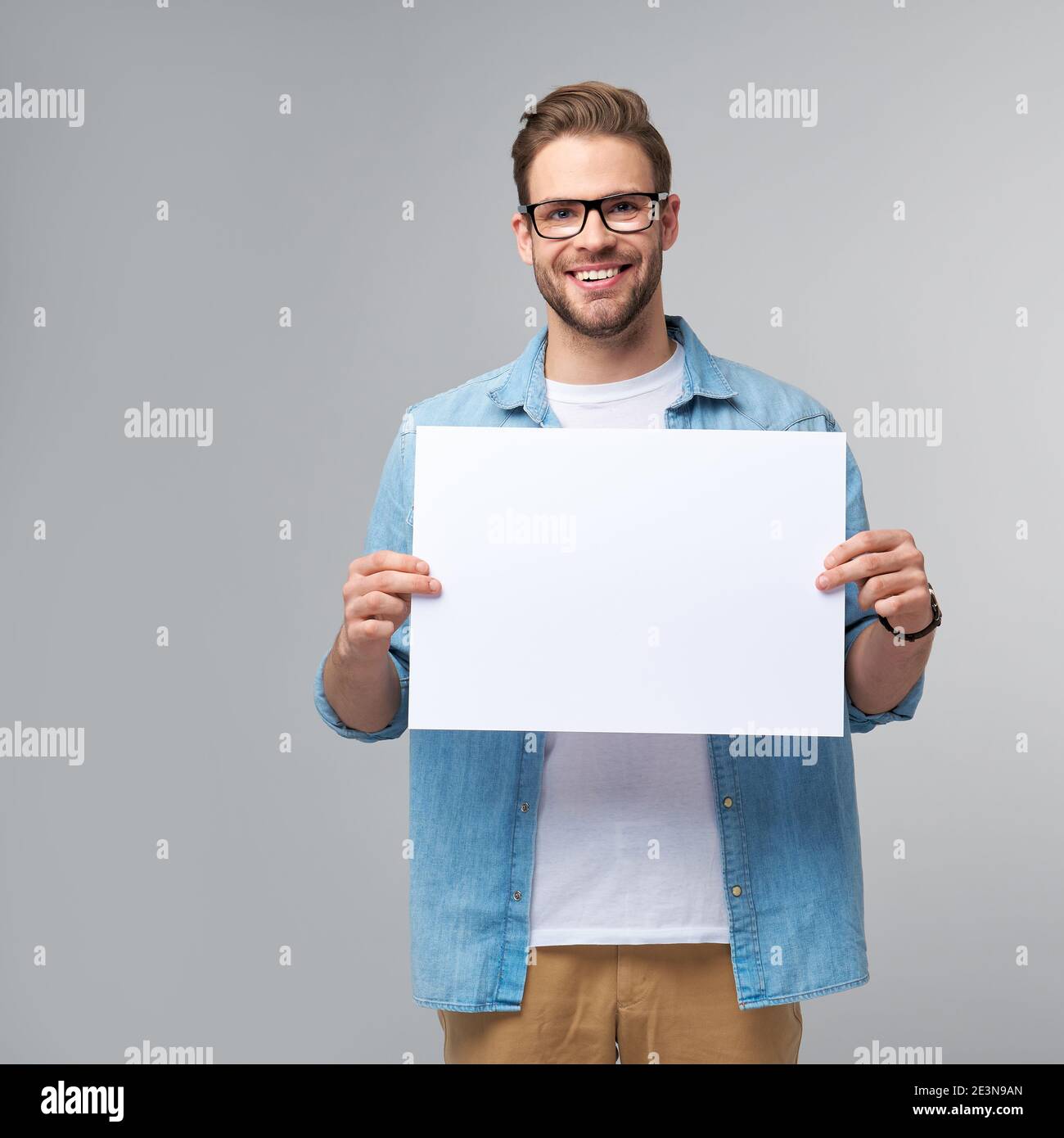 Portrait of a happy handsome young man holding blank white card or sign ...