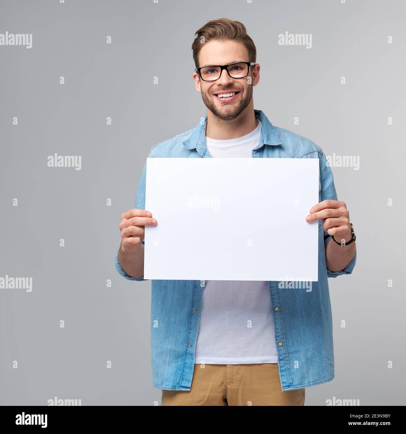 Portrait of a happy handsome young man holding blank white card or sign ...