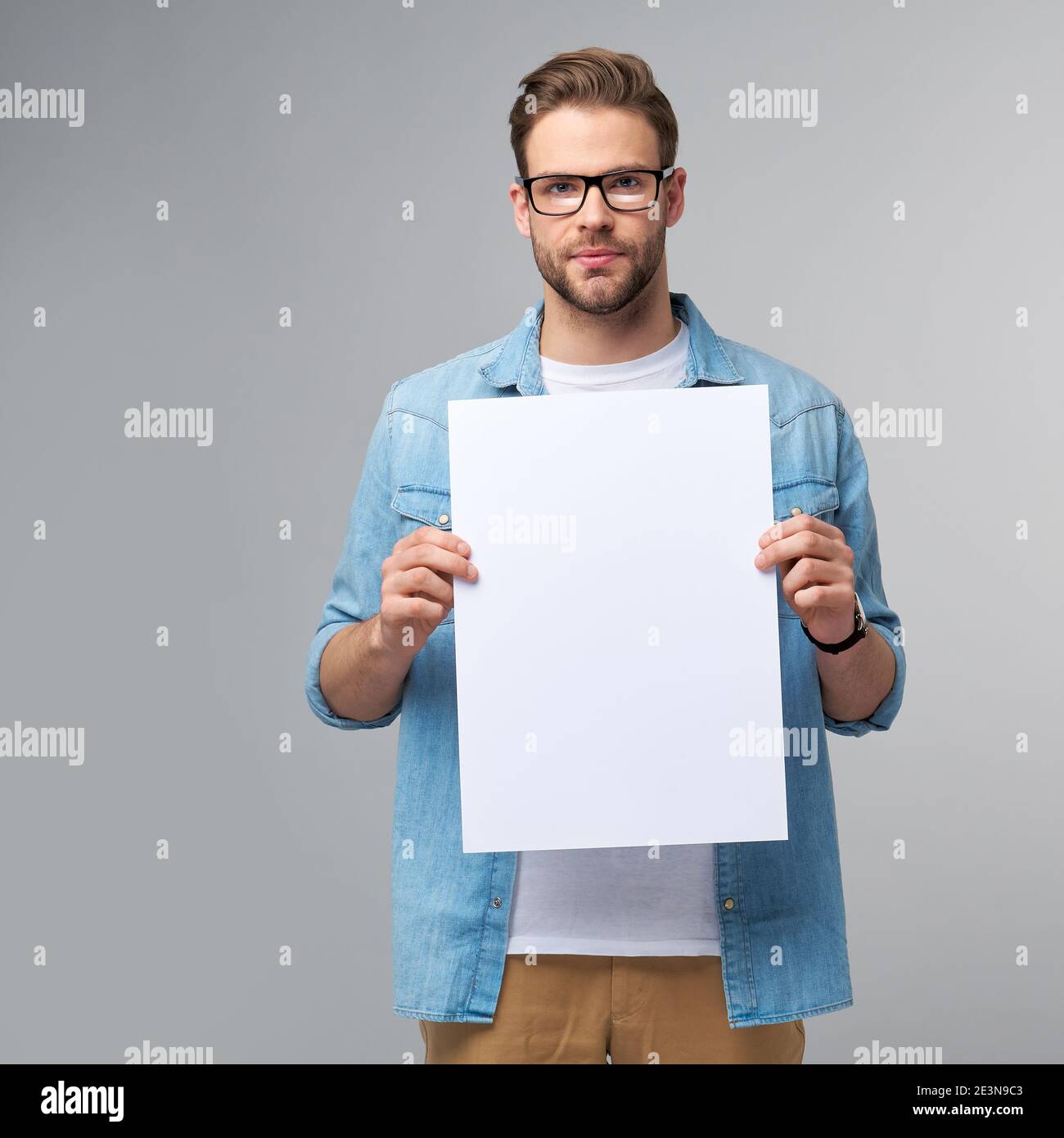Portrait of a happy handsome young man holding blank white card or sign ...