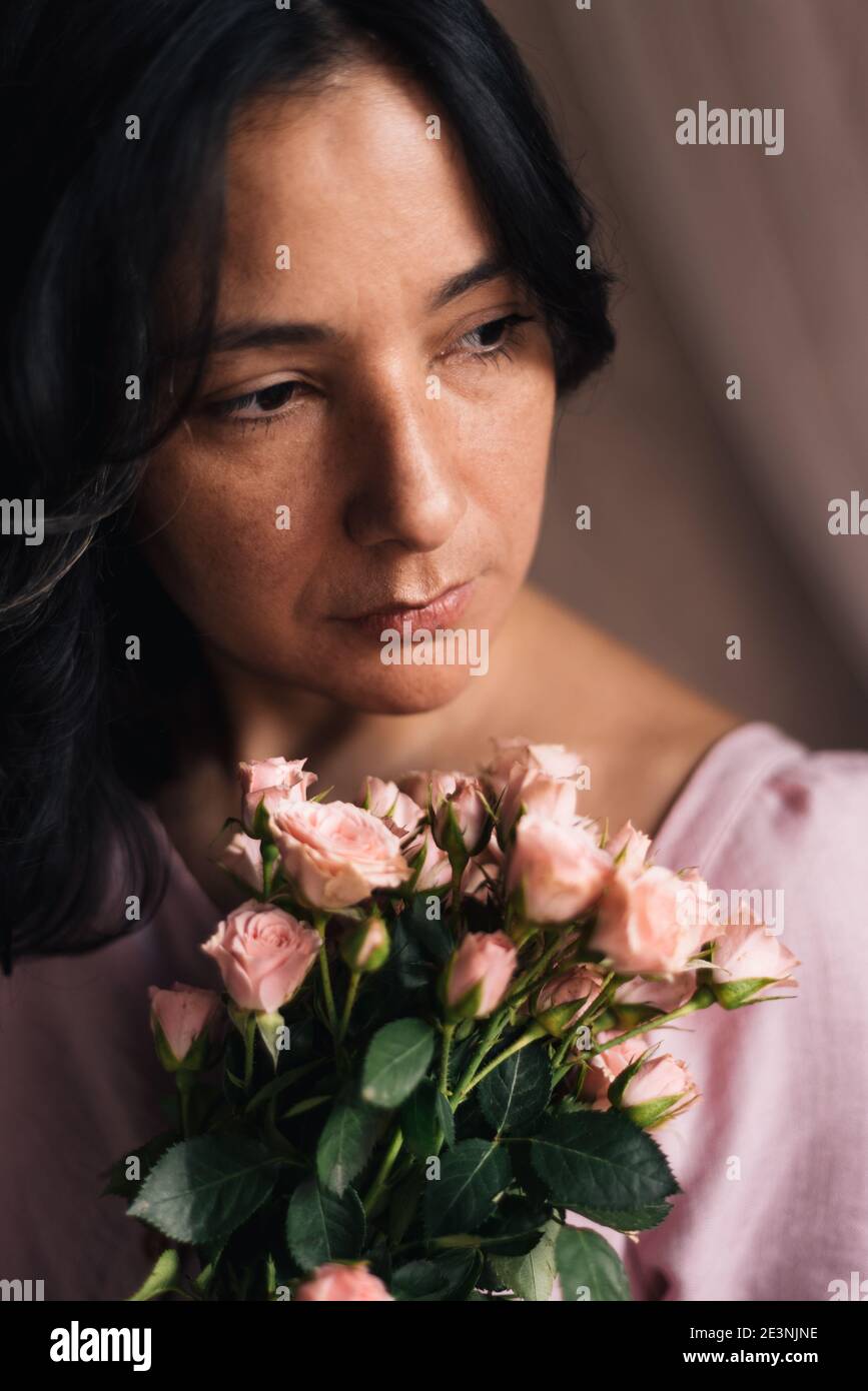 young thirtysomething woman portrait with pink roses and natural light vertical close up. concept of midlife sophisticated woman. confident femininity Stock Photo