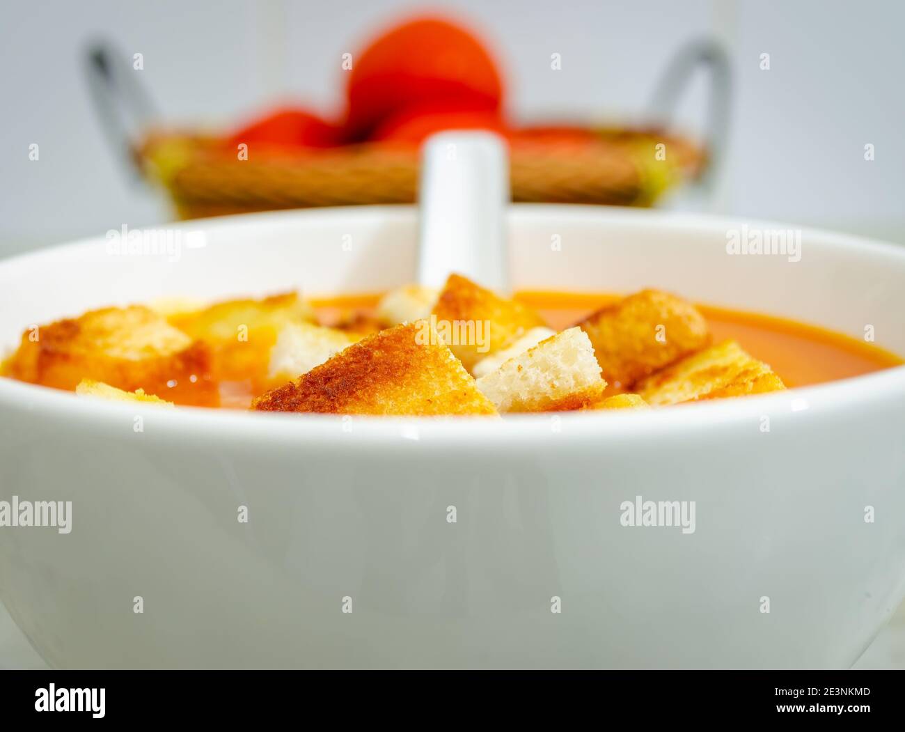 Beautiful View of Tomato Soup with bread croutons in a bowl with soup spoon and tomatoes in a basket in the background Stock Photo