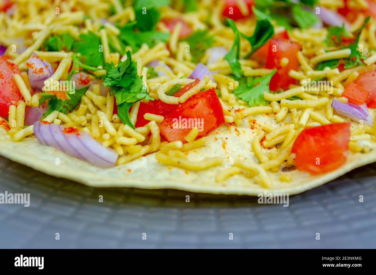 North Indian Snacks Masala Papad spread with sev, tomato, onions and Coriander leaves Stock Photo