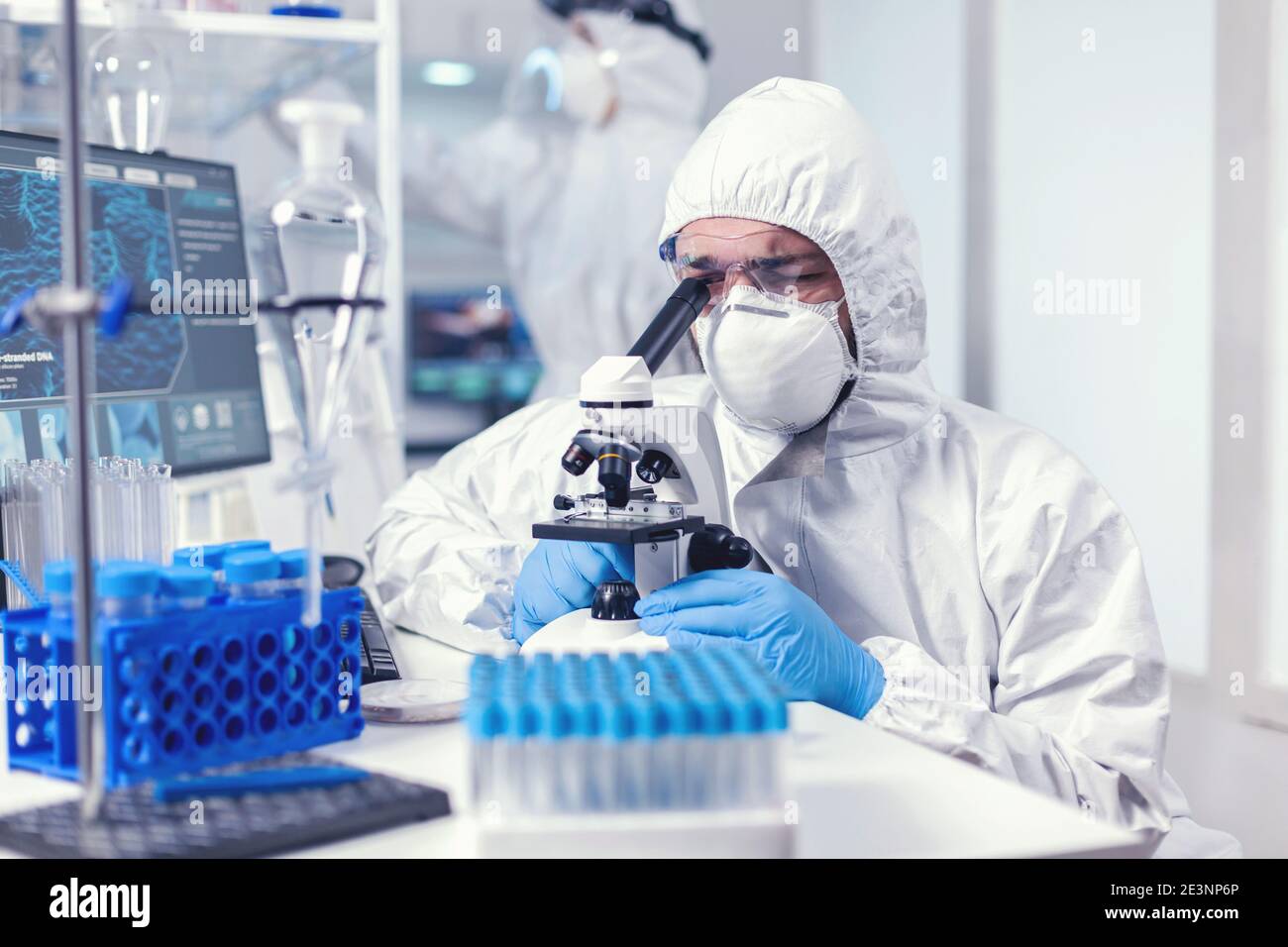 Lab technician in ppe gear examining virus samples under microscope in