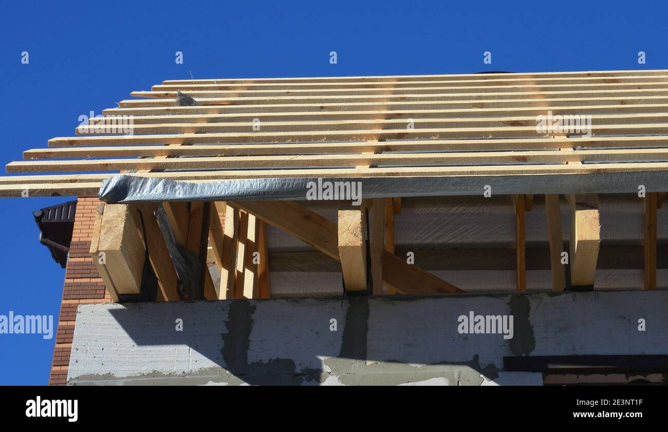 Unfinished roofing construction with a close-up on ceiling joists, wooden rafters, beams, and roof sheathing on a vapor barrier of a gable roof. Stock Photo