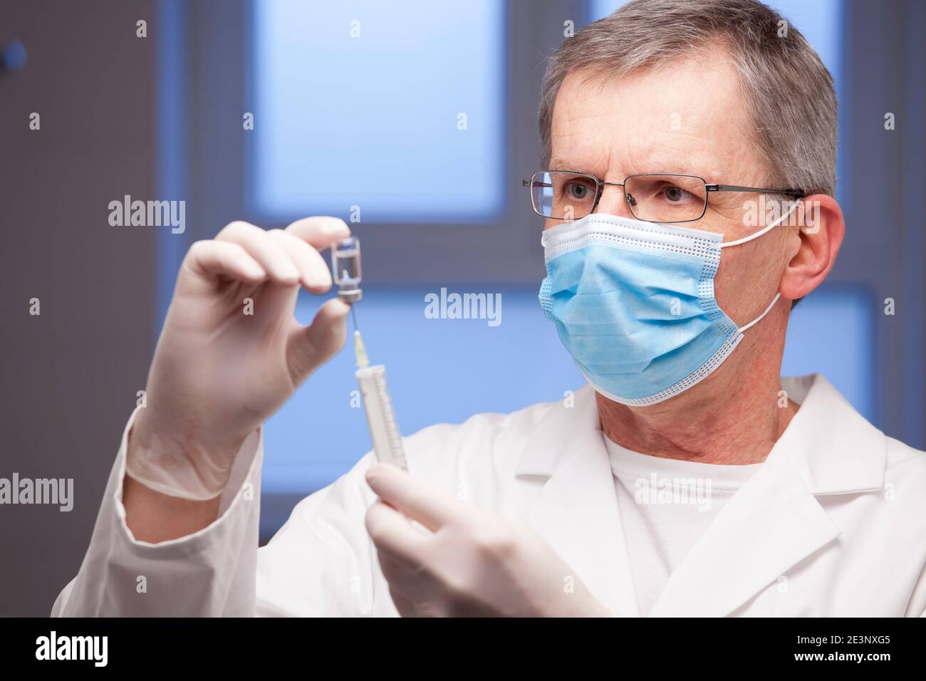 Doctor with medical mask preparing a syringe for vaccination against covid-19 - focus on the face Stock Photo