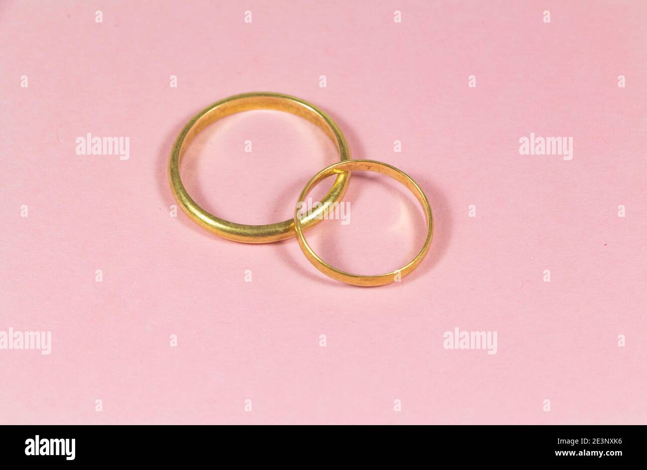 Two wedding rings made in gold on pink background Stock Photo - Alamy