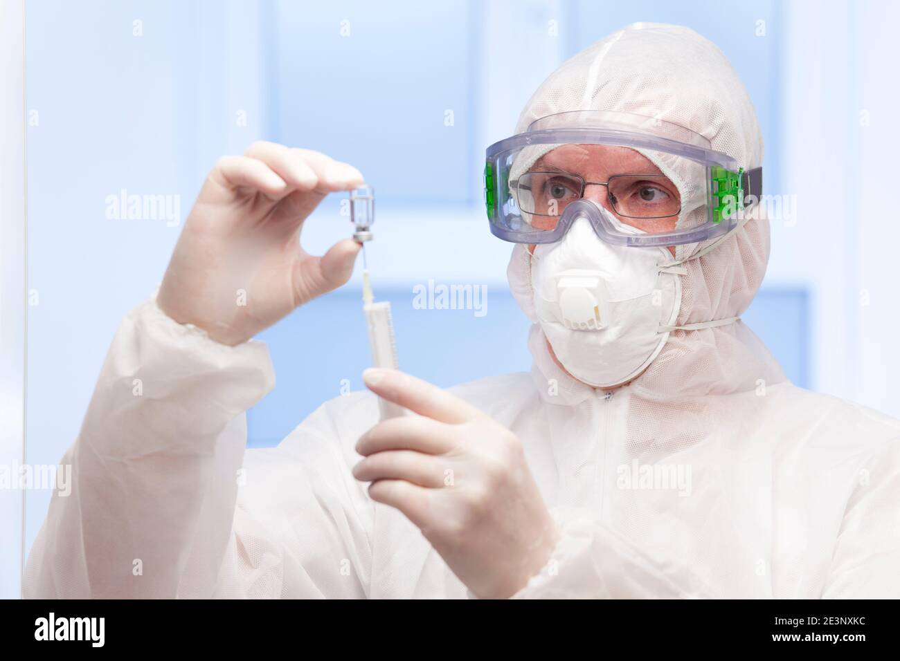 Doctor in white protective clothing and medical mask preparing a syringe for vaccination against covid-19 - focus on the face Stock Photo