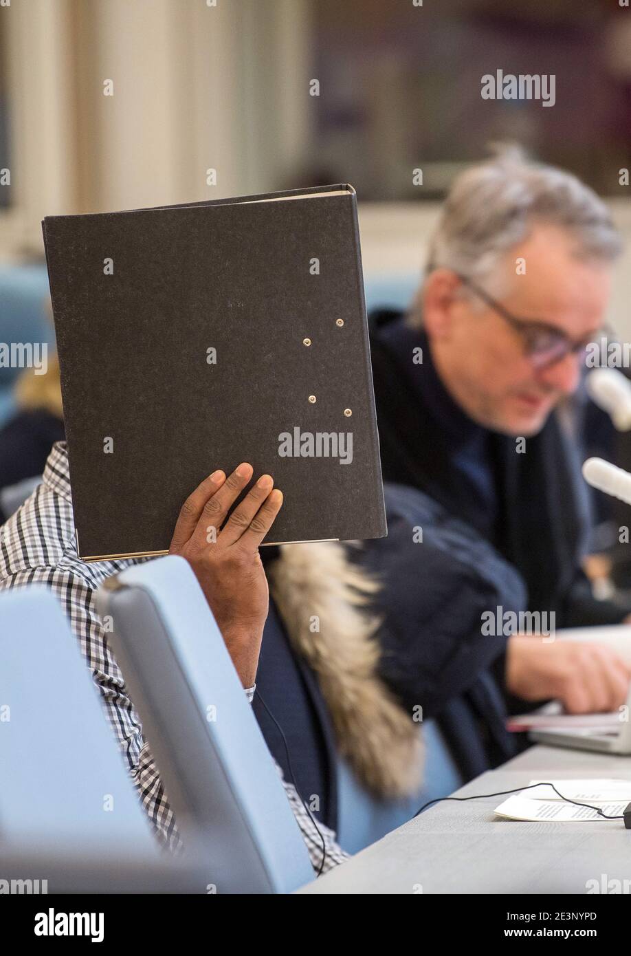 Duesseldorf, Germany. 20th Jan, 2021. The defendant holds a file folder in front of his face in the courtroom of the Higher Regional Court. Next to him sits his lawyer, Christoph Wingerter. The man is charged with murder and is alleged to have remotely detonated a bomb in front of a Sri Lankan army convoy when he was 15 years old in Sri Lanka. Six people are said to have been killed and many others injured in the attack a good twelve years ago. Credit: Federico Gambarini/dpa/Alamy Live News Stock Photo