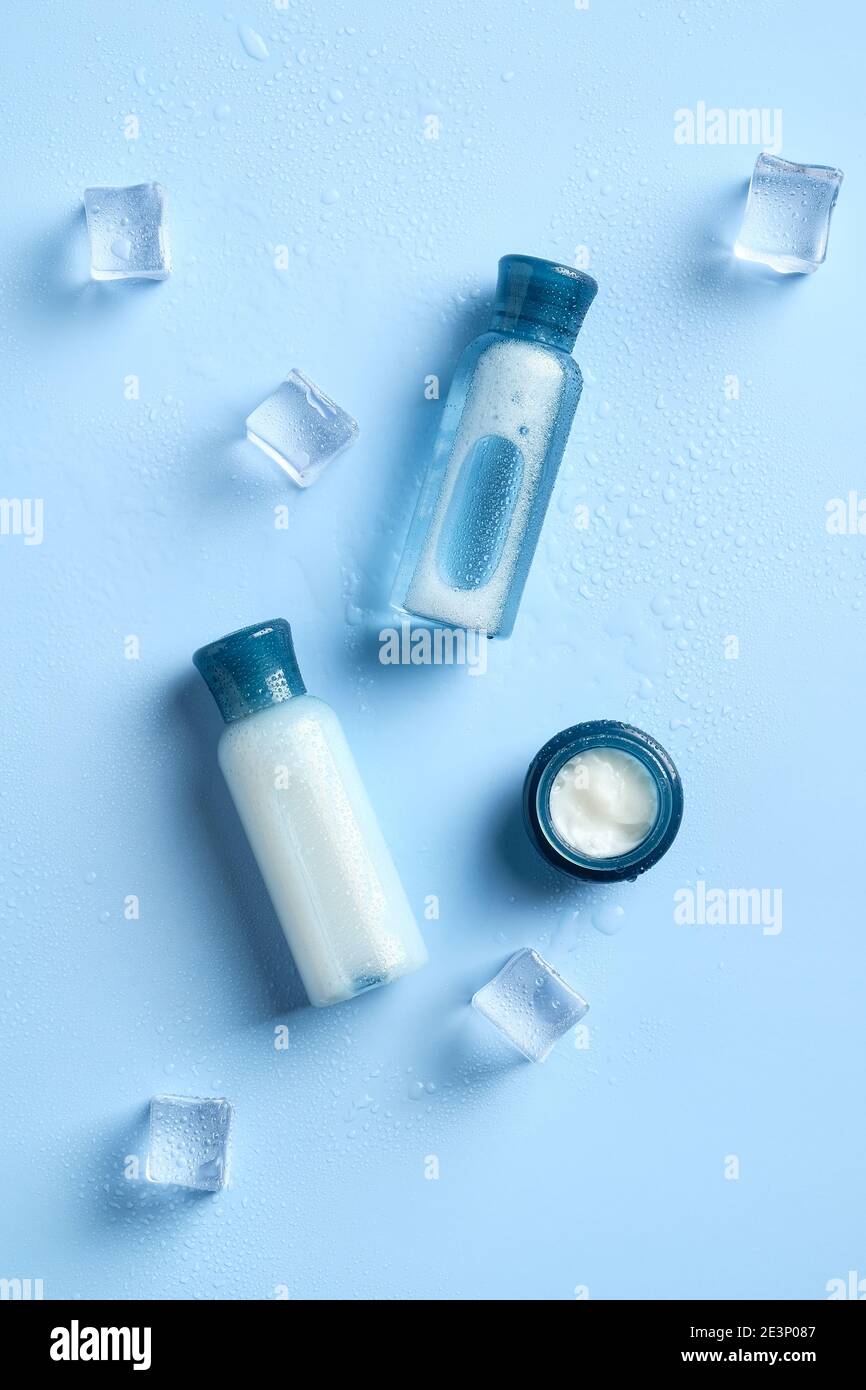 Moisturizing lotions and jar of cream on blue background with ice cubes