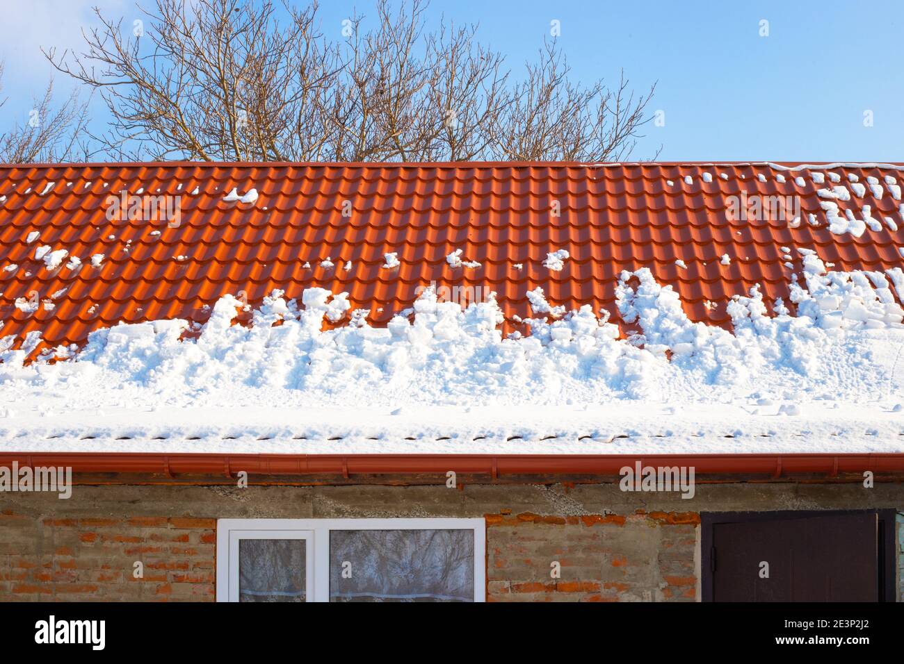 Metal roof in the snow in winter. Descent of snow avalanches from rooftops. Stock Photo
