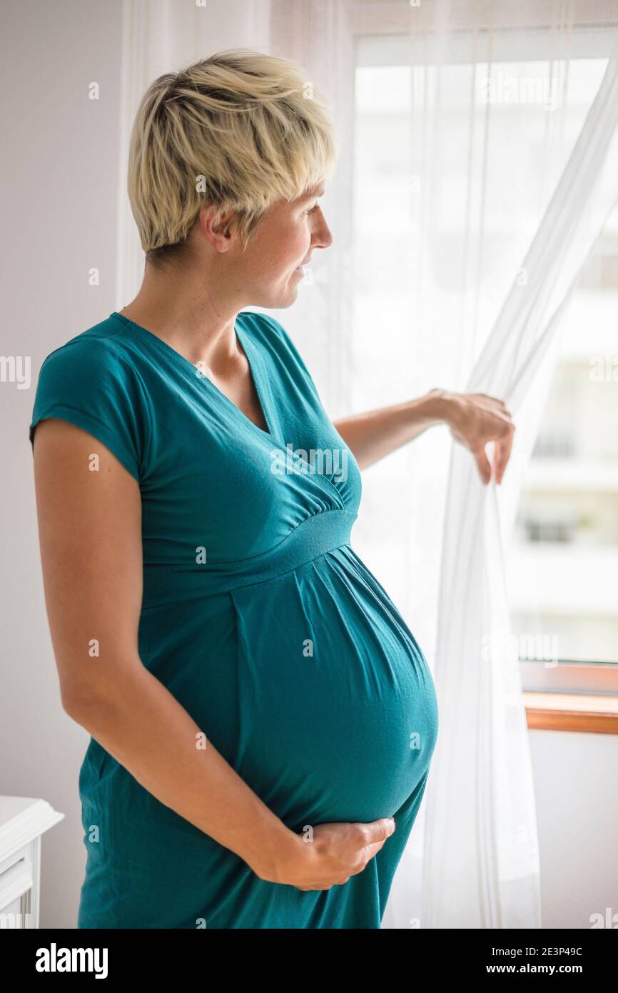 Pregnant woman with big belly looking through the window Stock Photo