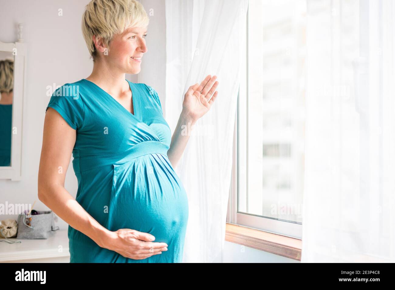Pregnant woman with big belly looking through the window Stock Photo