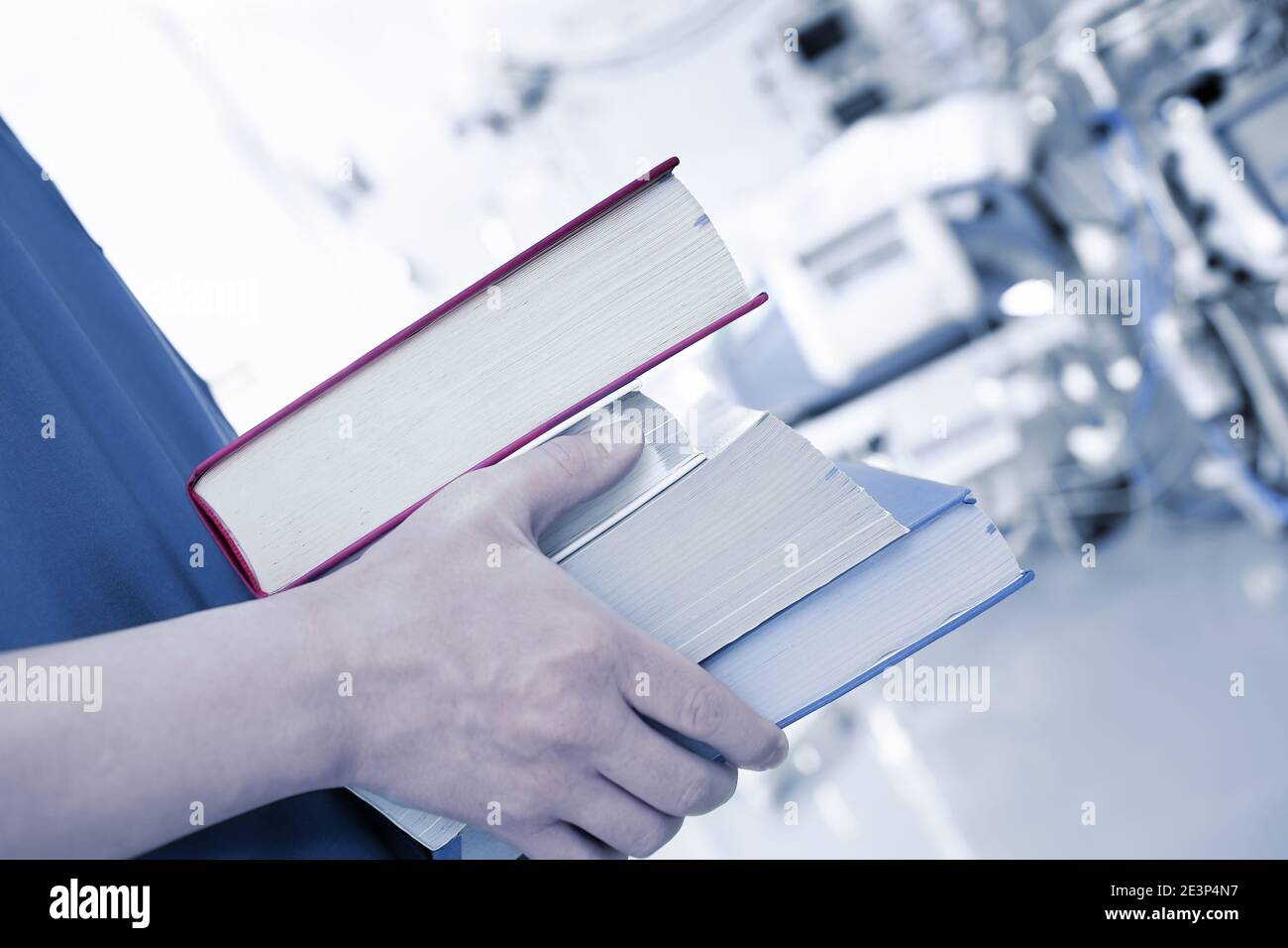 Books stacked in the hands of a young specialist in a room with equipment Stock Photo