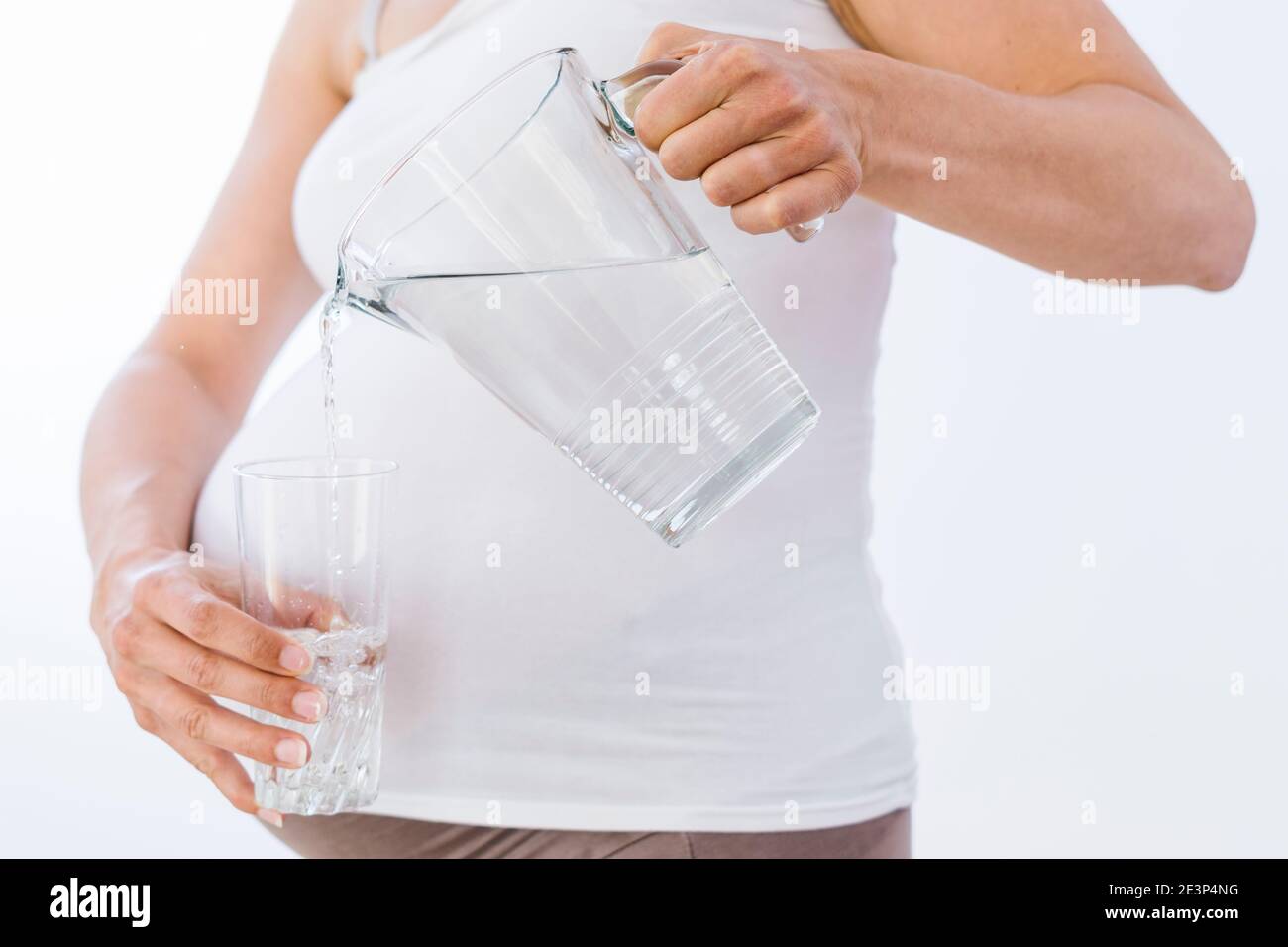 Pregnant woman pouring water from the jar to the glass on white background Stock Photo