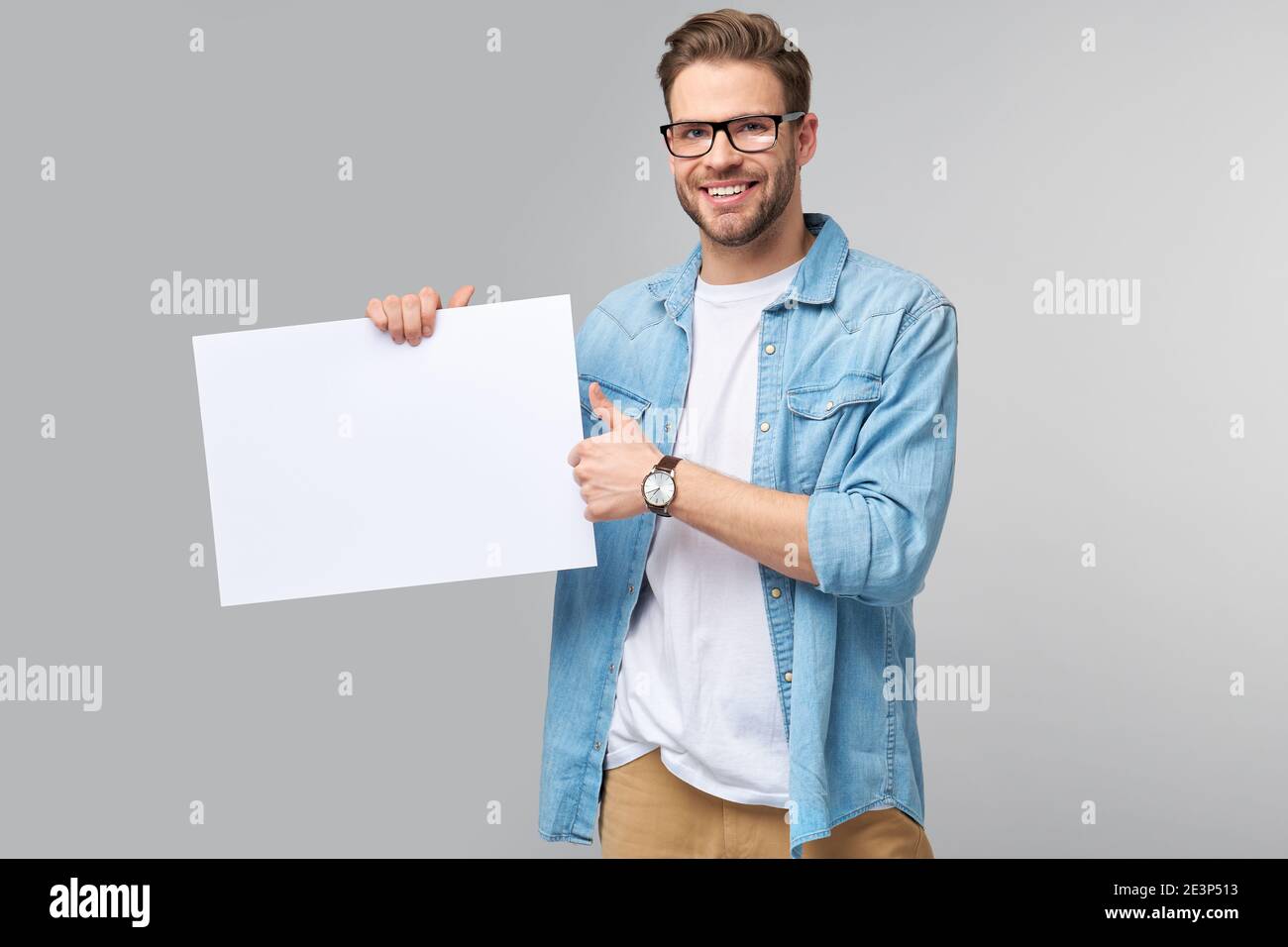 Portrait of a happy handsome young man holding blank white card or sign ...